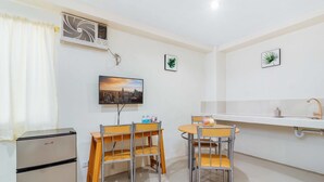 A compact kitchen with a refrigerator, two wooden chairs, a small table, a wall-mounted TV, and a sink with a faucet. - RedDoorz @ Salinas Extension Lahug (Cebu City)
