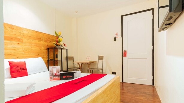 A hotel room with a wooden headboard, a bed with white bedding and a red accent, a small table with chairs, and a door with a 'No Entry' sign. - RedDoorz @ Vicente Street Espana Manila (Manila)