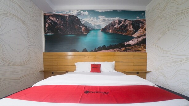 Une chambre d’hôtel avec une grande fresque murale représentant un paysage de montagne, une tête de lit en bois et une couverture de lit rouge.