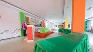 Un hall d’hôtel avec un comptoir d’accueil, des piliers verts et orange, et un espace aménagé en scène.
