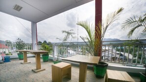 Un espace extérieur abrité, doté de tables et de chaises, de plantes en pot, et offrant une vue sur les bâtiments et les montagnes.
