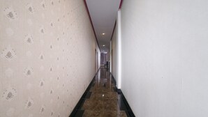 Un long couloir étroit, avec un papier peint à motifs sur un côté et des murs unis de l’autre, qui mène à une porte au bout.
