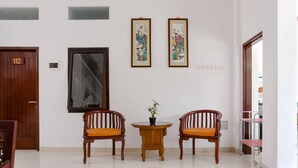 A hotel lobby with two wooden chairs, a small table with a vase, and two framed artworks on the wall. - RedDoorz near Jawa Timur Park 3 (Batu)