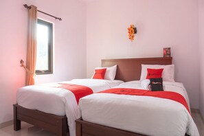 Una habitación de hotel con dos camas, cada una con ropa de cama blanca y detalles en rojo, un cabecero de madera y una ventana con cortinas.