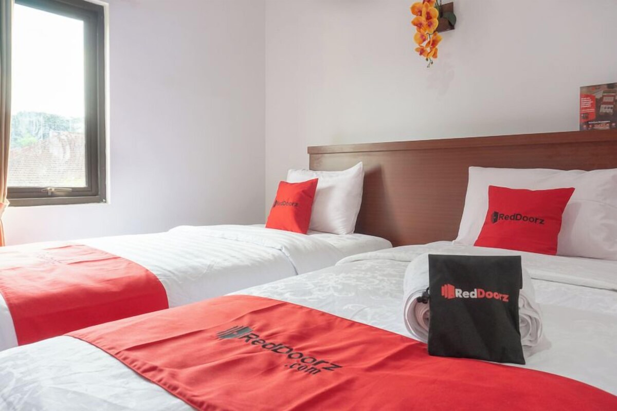 Quarto de hotel com duas camas, cada uma com colcha branca e vermelha, e travesseiros com o logotipo RedDoorz.