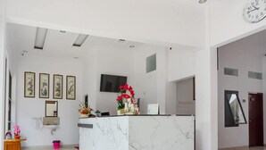 A modern reception area with a marble counter, a clock, framed artwork, and a TV mounted on the wall. - RedDoorz near Jawa Timur Park 3 (Batu)