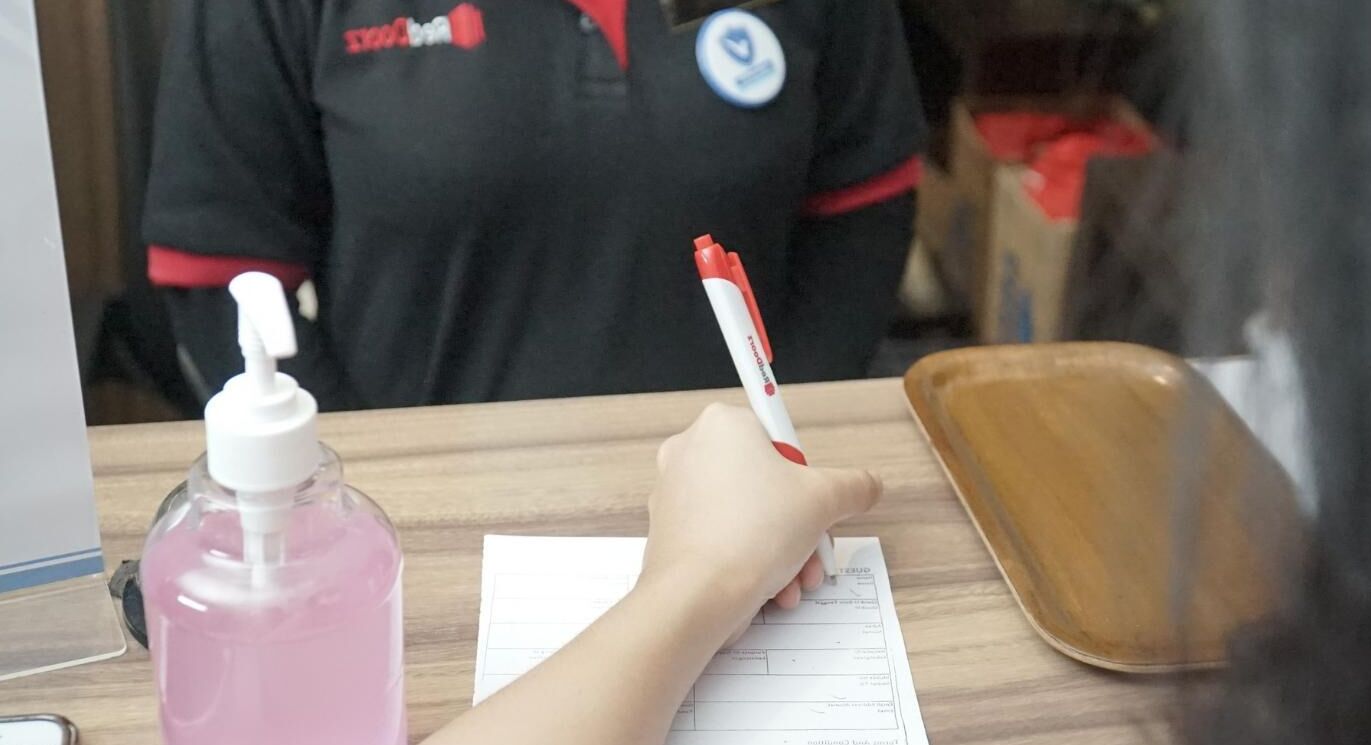 A person filling out a form at a counter with a pink bottle of hand sanitizer and a brown tray.