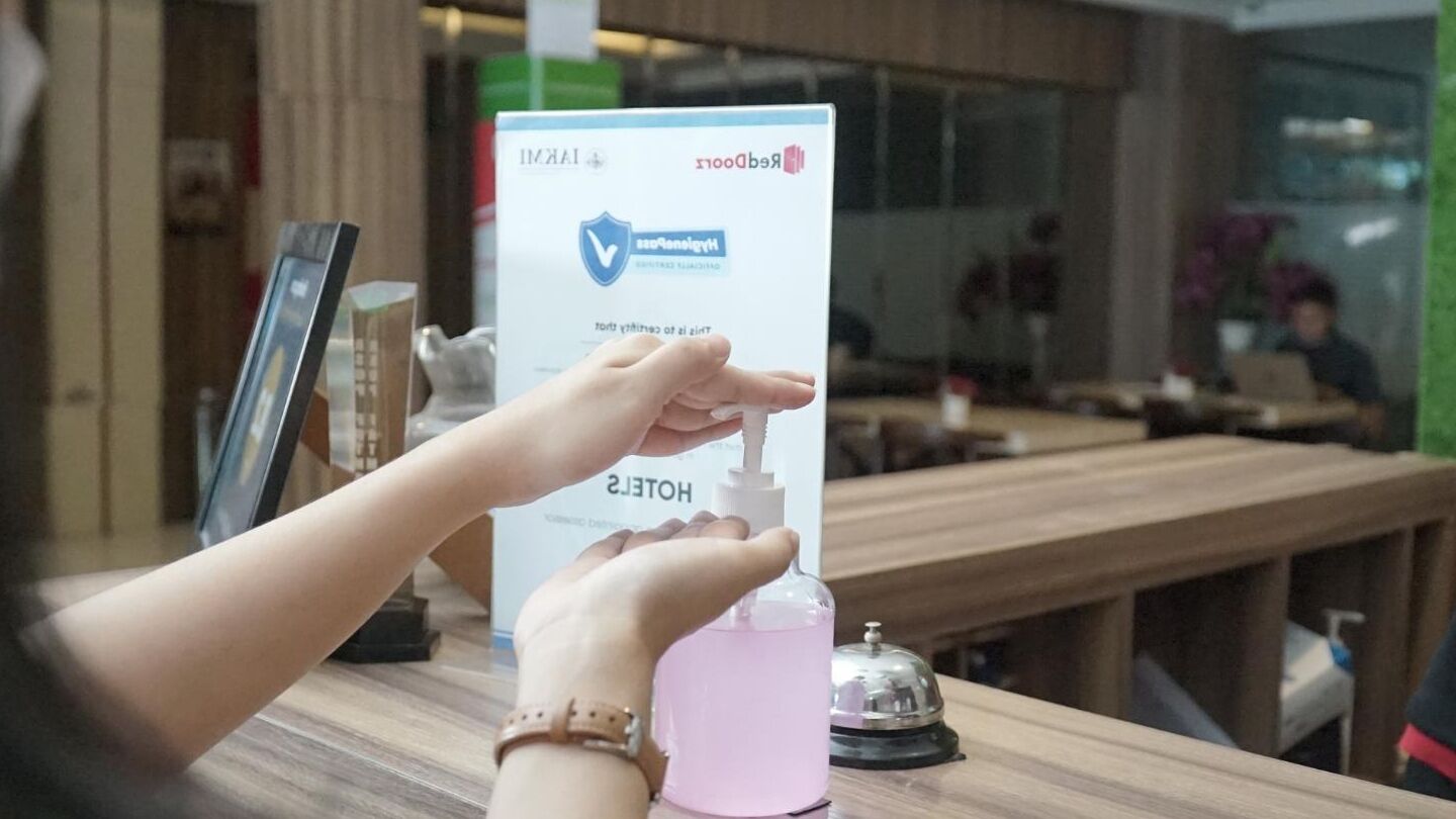 Una persona usando un dispensador de gel hidroalcohólico en la recepción de un hotel.