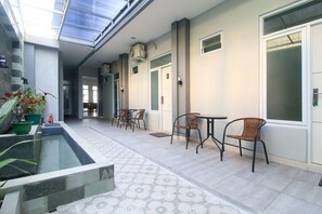 A corridor with a glass ceiling, a small pool, and seating areas with chairs and tables. - RedDoorz near Klaten Train Station (Klaten)