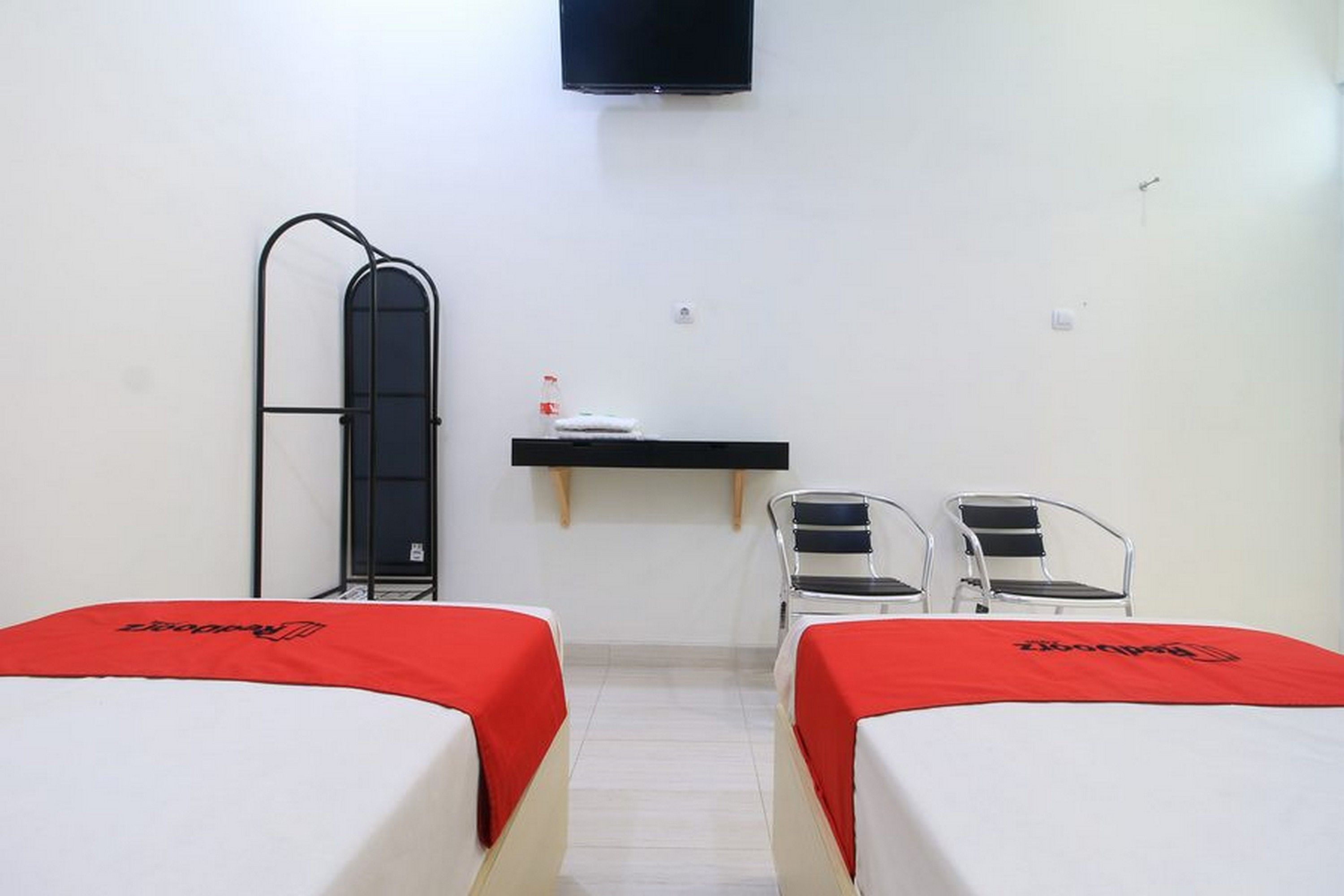 A hotel room with two beds, a desk, a chair, and a TV.