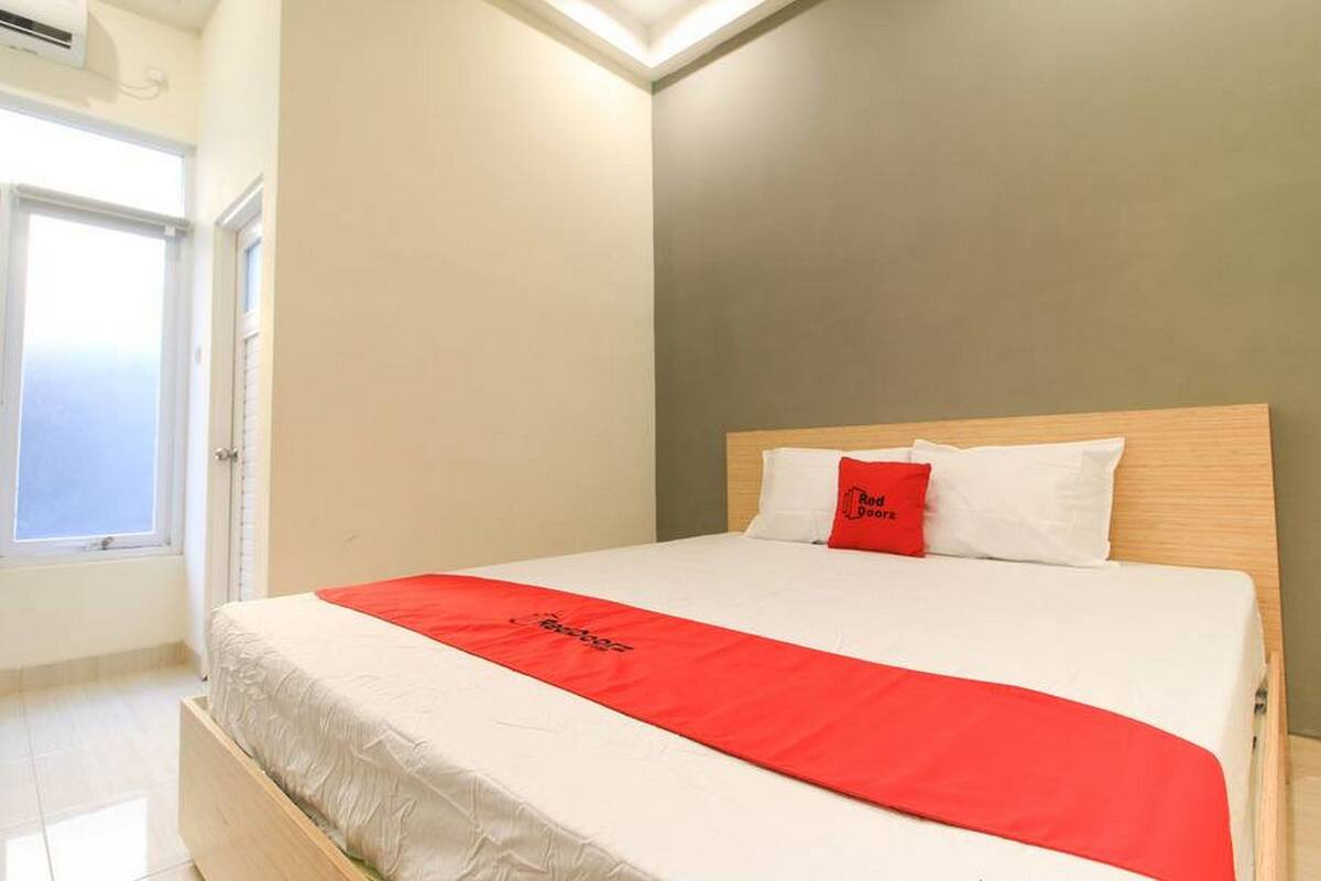 Een hotelkamer met een bed, een rode sprei en een raam met jaloezieën.