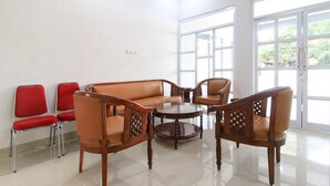 Une pièce comprenant un canapé, deux fauteuils et une table basse. Deux chaises rouges sont placées contre le mur.