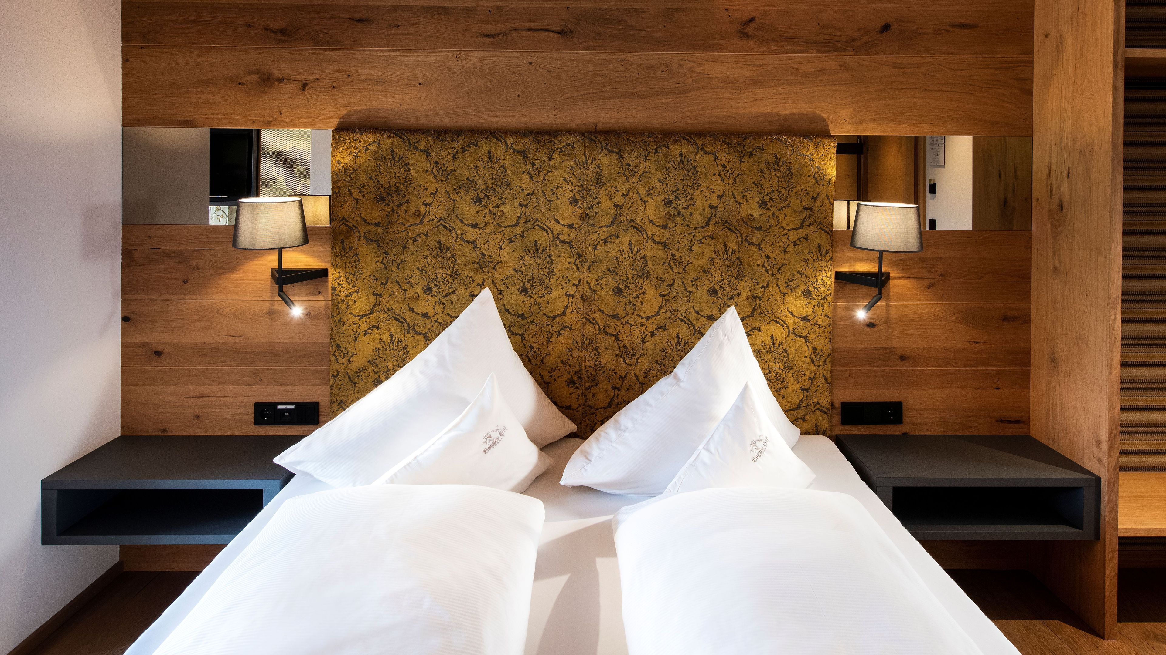 Ein Hotelzimmer mit einem hölzernen Kopfteil, zwei Nachttischlampen, einem Bett mit weißer Bettwäsche und einem kleinen Nachttisch.