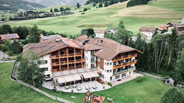 A large, multi-story building with a traditional Alpine architectural style, surrounded by lush green fields and mountains in the background. - Rossalpe - Hotel Bogner Hof (Bogen)