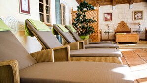 A row of wicker lounge chairs with cushions, a wooden bed, a potted plant, and a wall-mounted shelf with a lamp. - Rossalpe - Hotel Bogner Hof (Bogen)