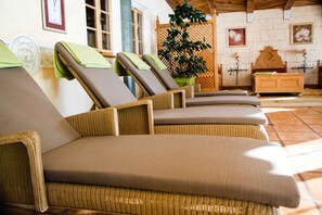 A row of wicker lounge chairs with cushions, a wooden bed, a potted plant, and a wall-mounted shelf with a lamp. - Rossalpe - Hotel Bogner Hof (Bogen)