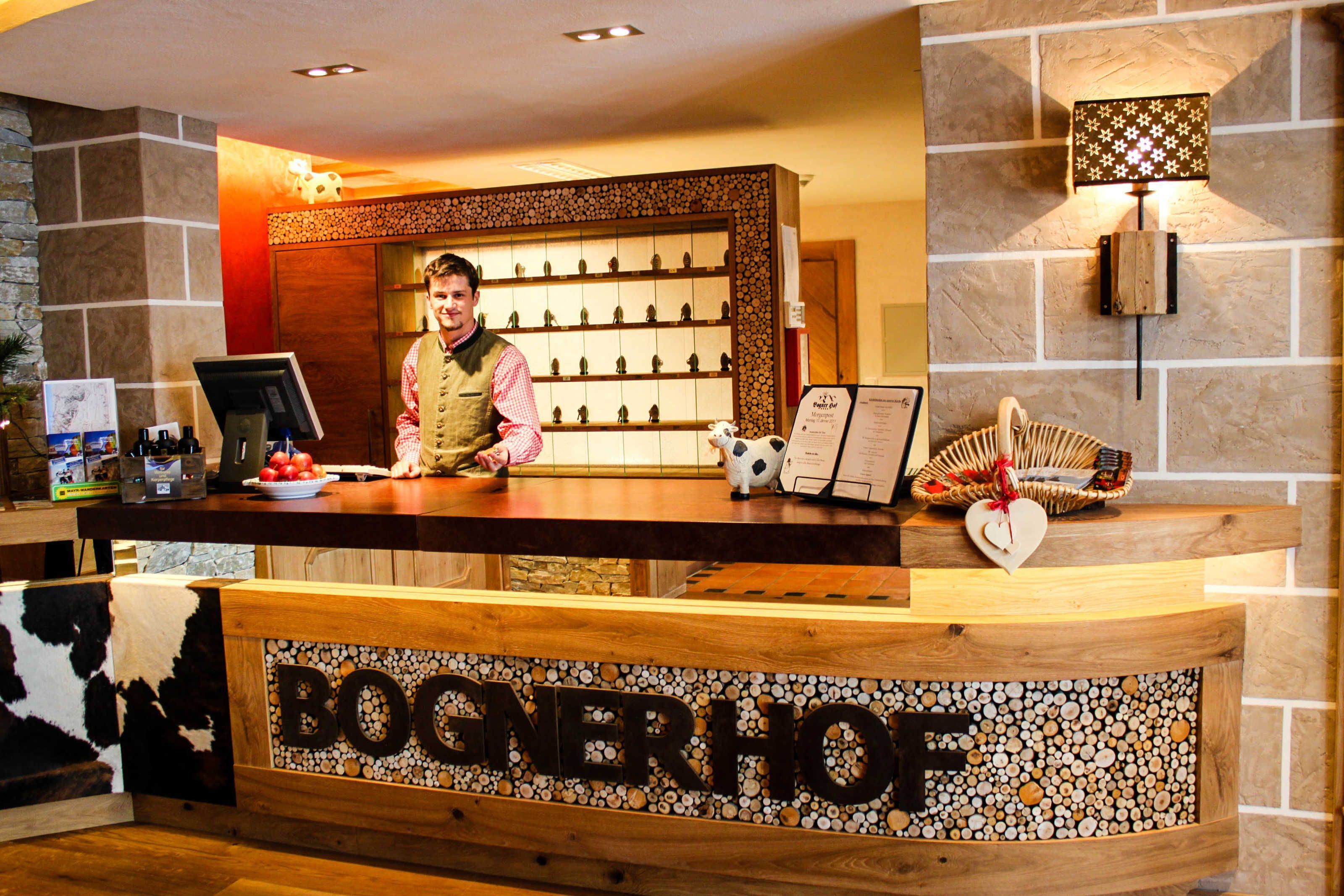 En receptionsdisk med en skylt som visar texten ”BOGNERHOF”, ett bord med ett urval av små figurer, en korg med ett hjärtformat föremål och en väggmonterad lampa.