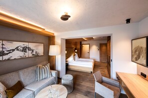A modern hotel room with a wooden ceiling, a bed, a sofa, a desk, and a painting on the wall.