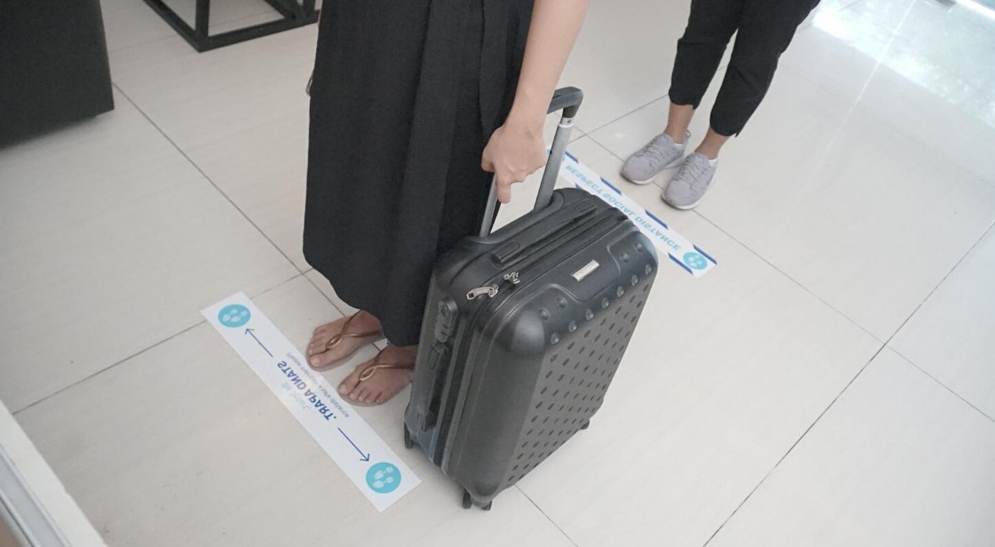 A person with a suitcase standing on a tiled floor with directional signs.