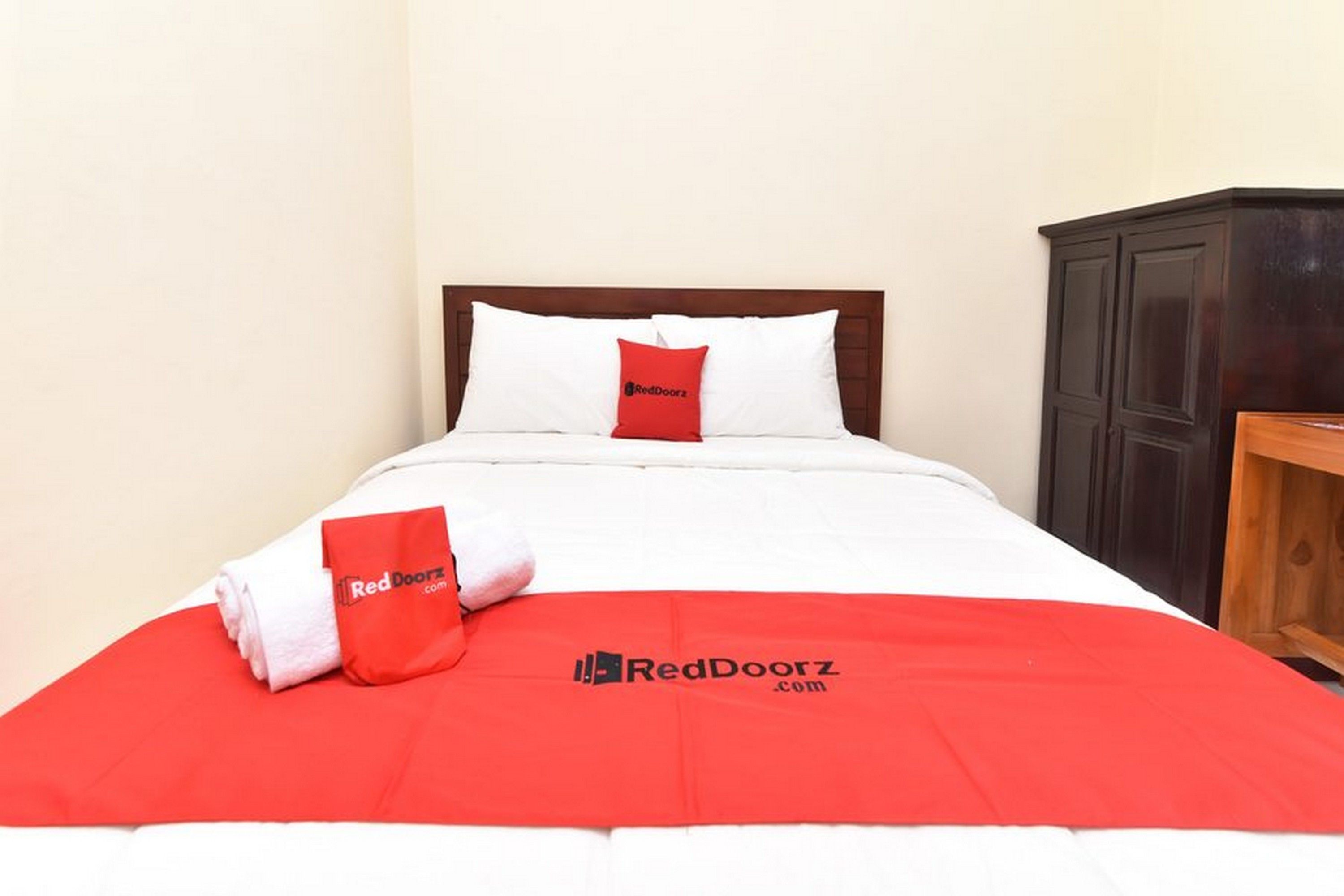 A neatly made bed with white and red bedding, a red pillow, and a red blanket with the RedDoorz logo.