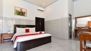 Une chambre d’hôtel avec un grand lit, une table de chevet en bois, un bureau avec une chaise et une salle de bain visible à travers une porte ouverte.