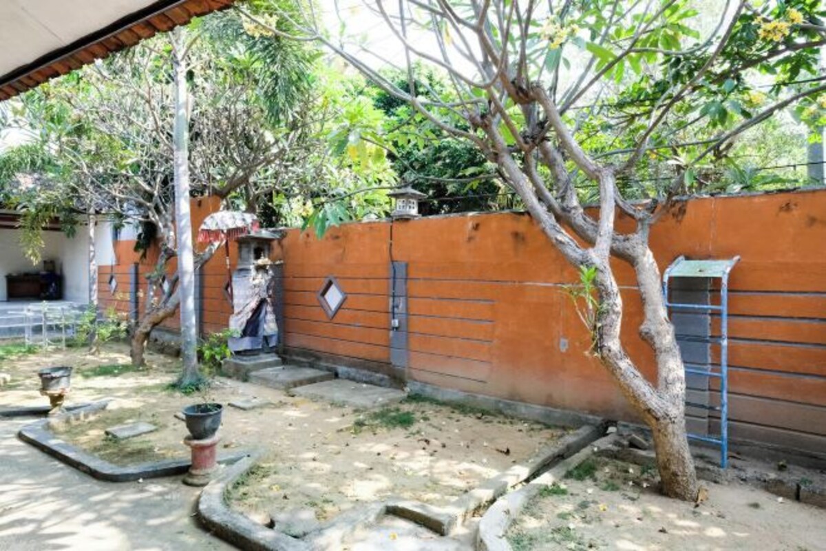 Un patio con un árbol, un muro de ladrillo y una reja de metal.