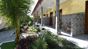 Un bâtiment doté d’un espace extérieur abrité, de piliers en pierre et d’un jardin où poussent différentes espèces de plantes.
