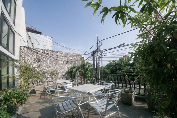 An outdoor patio with metal chairs and tables, surrounded by potted plants and a decorative fence. - RedDoorz Plus near Green Pramuka Square Mall (Jakarta)