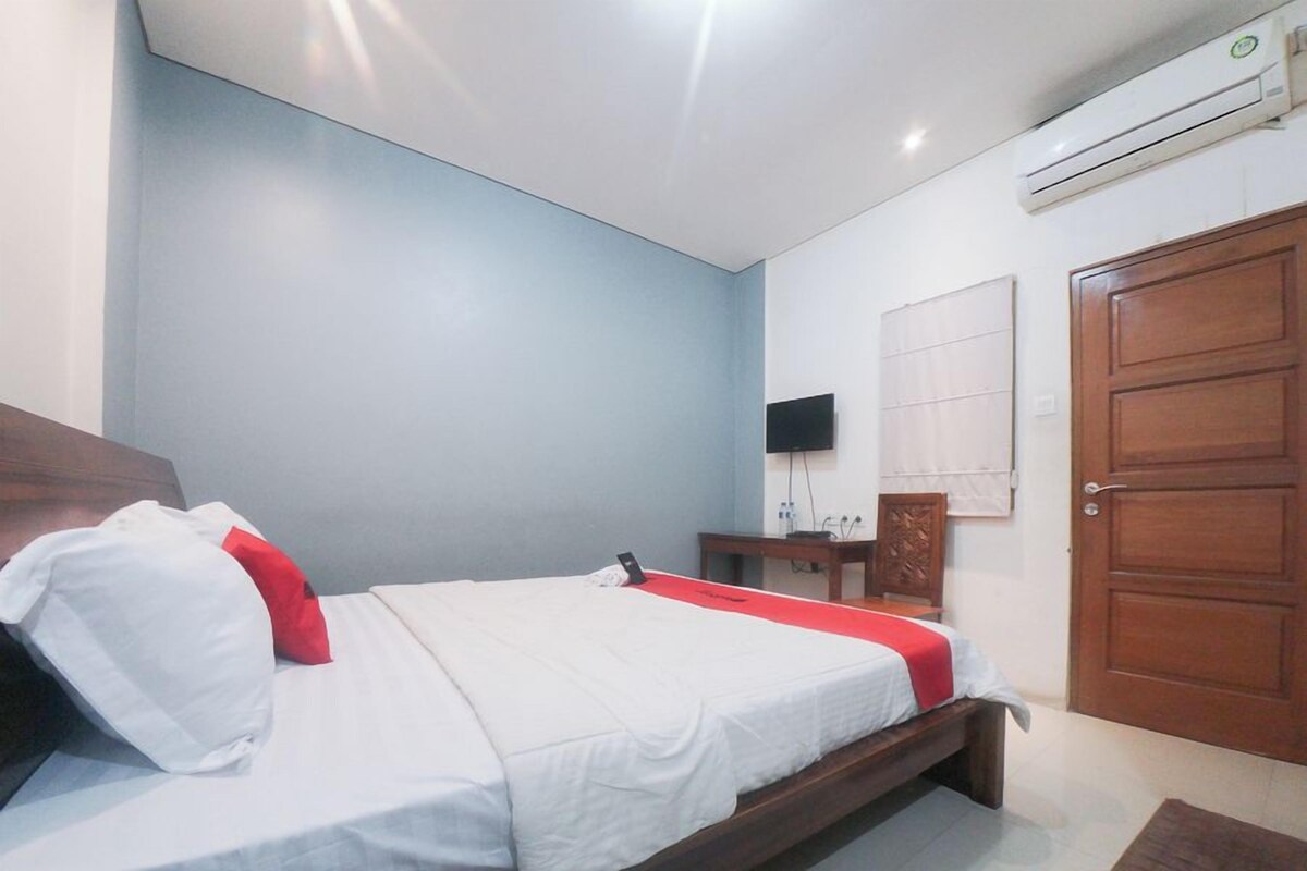 Une chambre à coucher avec un lit, une porte en bois, un téléviseur fixé au mur et un appareil de climatisation.