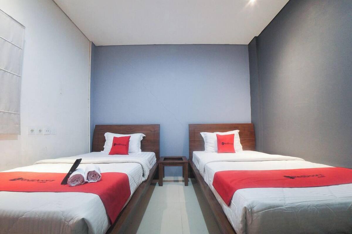 A hotel room with two beds, each with a red bedspread and white bedding, a wooden headboard, and a small table between the beds.