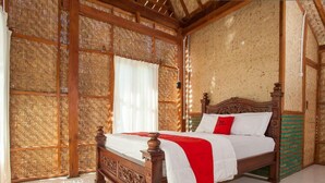 Una cama de madera con una colcha roja y blanca en una habitación con un muro tejido y suelo de baldosas.