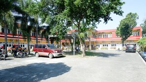 A courtyard with a red and yellow building, a covered seating area, and parked vehicles.