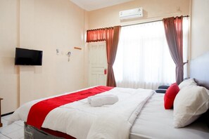 A hotel room with a bed, a flat-screen TV mounted on the wall, and a window with curtains.