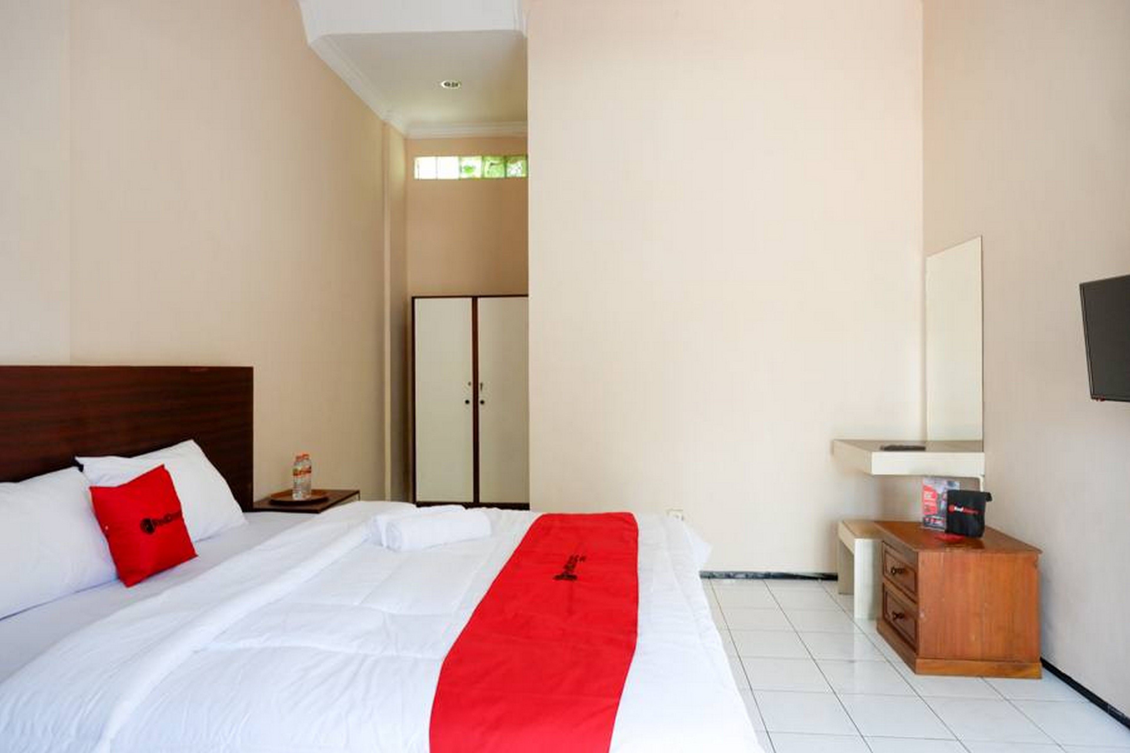A hotel room with a bed, a wooden nightstand, a mirror, and a wardrobe.