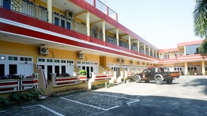 A multi-story building with a red and yellow facade, a parking area, and a rescue vehicle parked in front.
