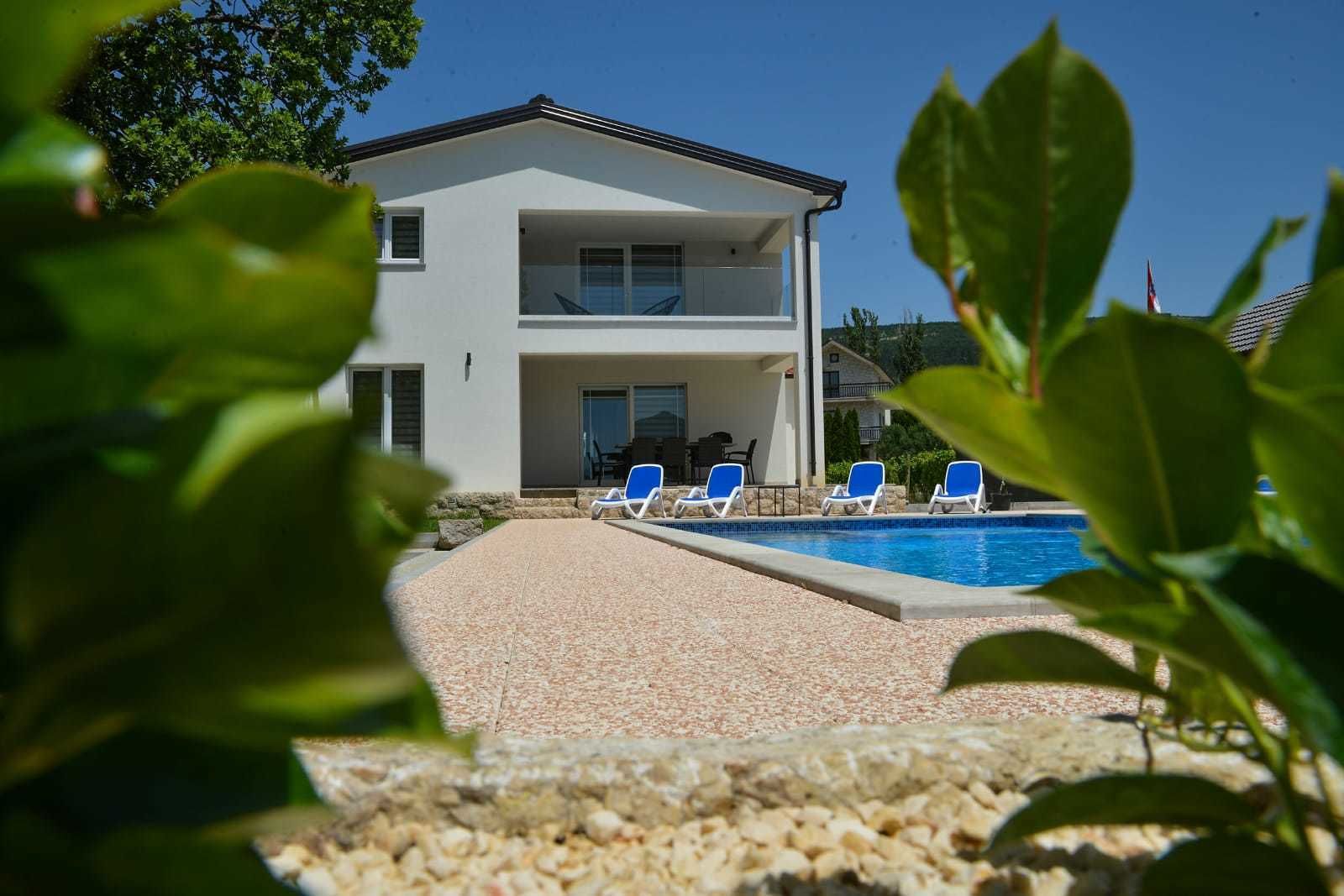 A two-story building with a swimming pool, surrounded by a gravel patio and blue lounge chairs.