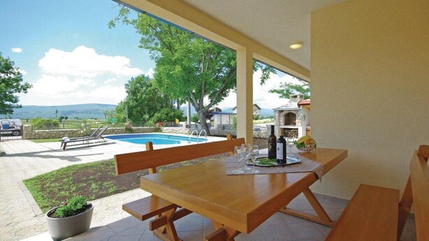 Una mesa de madera con un banco, una piscina y vistas al campo.