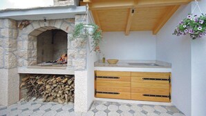 Cocina exterior de piedra con estufa de leña, una maceta colgante con flores y un mostrador de madera con cajones.