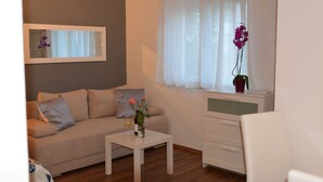 Uma sala de estar com sofá, mesa de centro, armário branco e janela com cortinas leves.