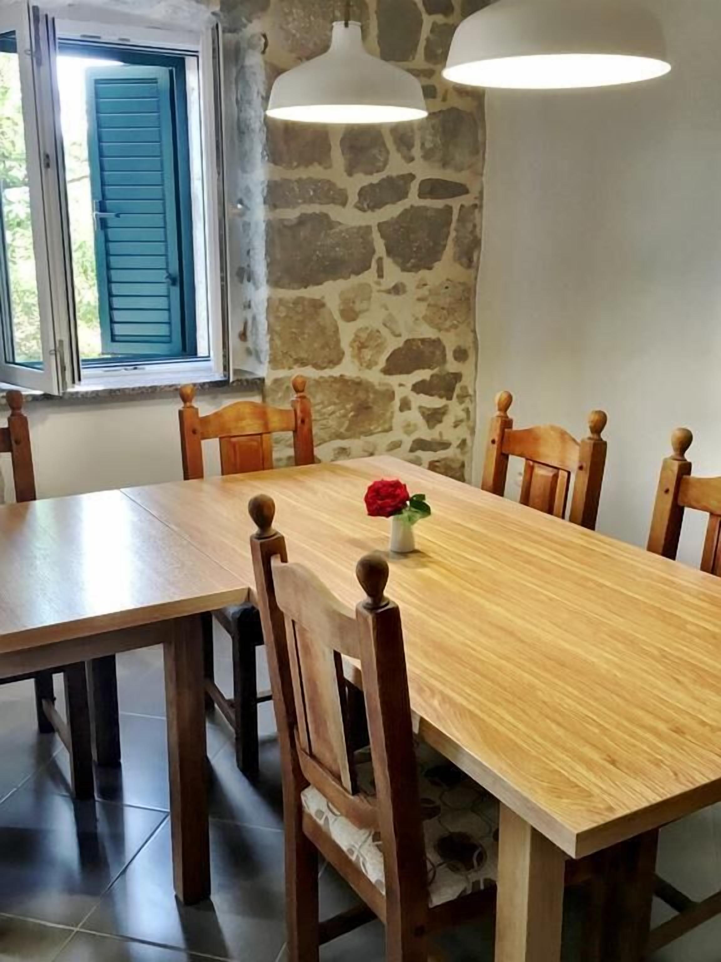 A dining area with a wooden table and chairs, stone wall, and two pendant lights.