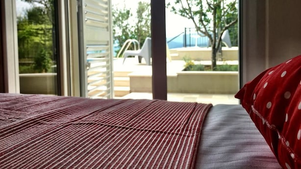 Un dormitorio con un ventanal grande, una cama con manta a rayas y vistas a muebles de exterior y vegetación.