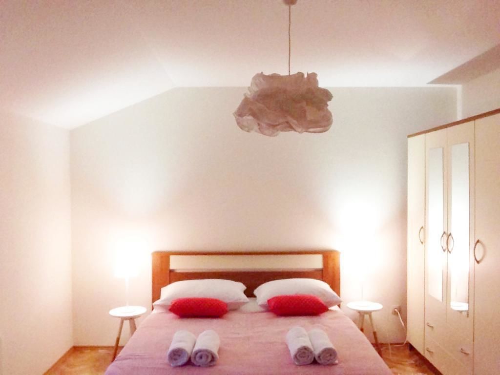 Un dormitorio con cabecera de madera, dos almohadas, dos mesitas de noche y una lámpara colgante.