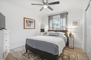 A bedroom with a bed, a ceiling fan, a nightstand, a lamp, a framed picture, and a dresser. - Amazing+Modern Coastal Resort+ Clearwater-Dunedin+ Pool+Backyard Oasis+Beaches (Dunedin)