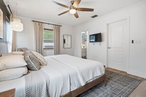 A bedroom with a bed, a ceiling fan, a television, and a door.