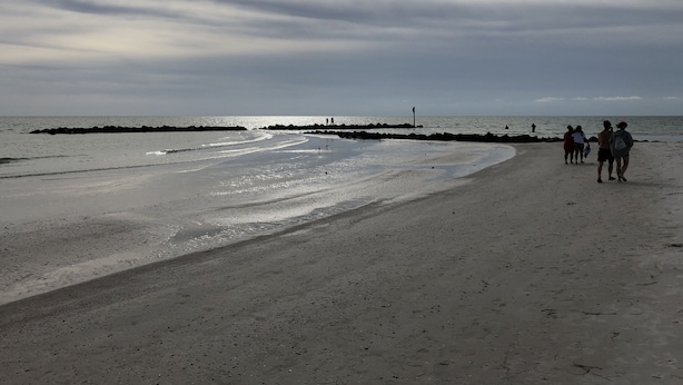 Una playa con un rompeolas rocoso y gente caminando por la orilla.