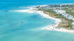 An aerial view of a coastal area with a beach, parking lots, and a road.