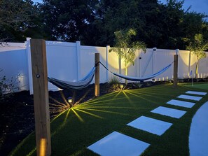 Un jardín con una hamaca, piedras para pisar y una valla blanca.