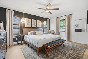 Un dormitorio con cama, mesitas de noche, un banco, ventilador de techo y obras de arte en las paredes.