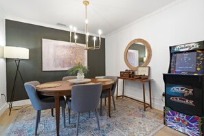 A dining area with a round table, chairs, a chandelier, a potted plant, a mirror, and a retro gaming console. - Amazing+Modern Coastal Resort+ Clearwater-Dunedin+ Pool+Backyard Oasis+Beaches (Dunedin)