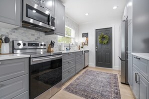 A modern kitchen with stainless steel appliances, grey cabinetry, and a patterned rug.